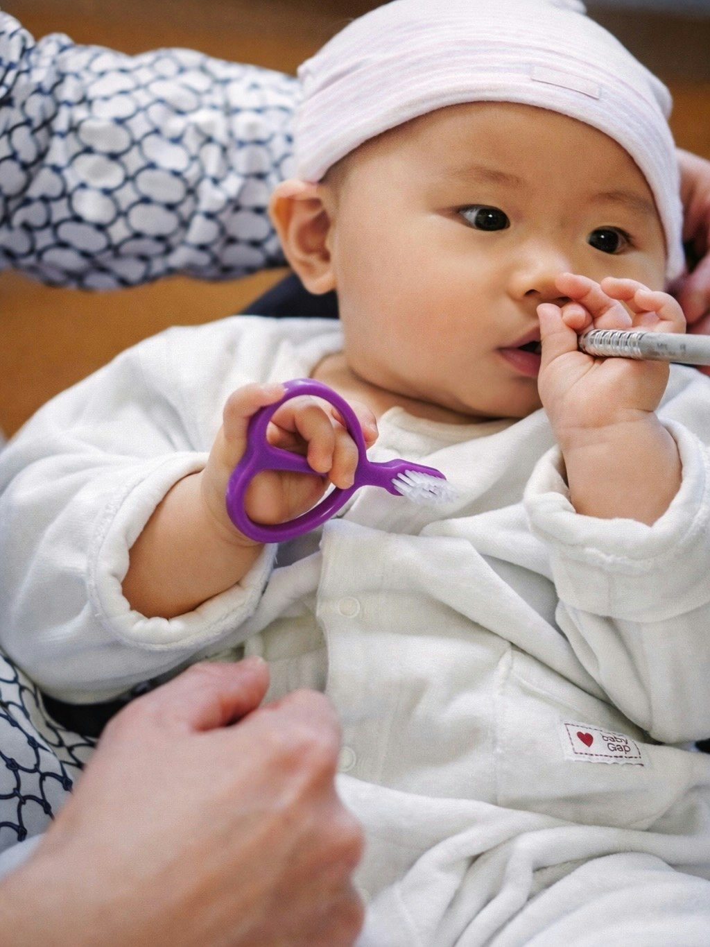 A baby at an early first dental visit, holding a training toothbrush
