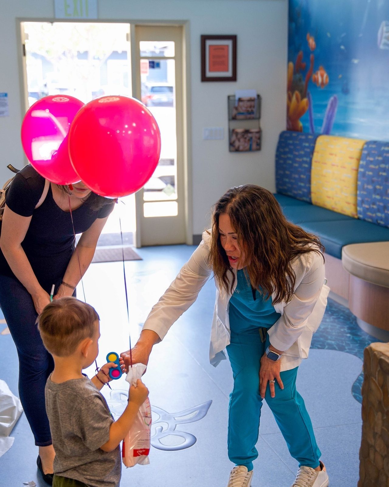 Dr. Tsai handing a young patient a prize in the balloon-filled waiting room